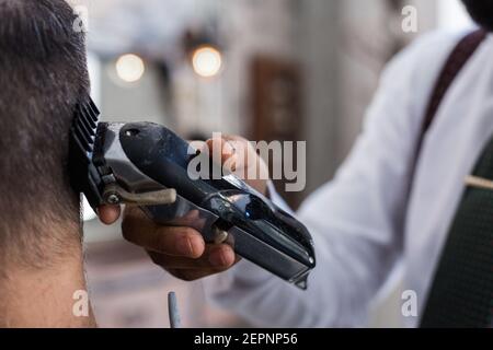 Nahaufnahme eines zugeschnittenen, nicht erkennbaren, stilvollen Dandy-Barbiers Trimmen Haare von erwachsenen Kunden mit elektrischen Haarschneider in Friseur Salon Stockfoto