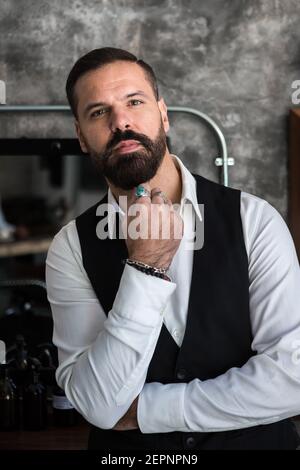 Erwachsene brutal männlich Exekutive in formelle tragen und Ringe berühren Bart beim Blick auf die Kamera im Friseursalon Stockfoto