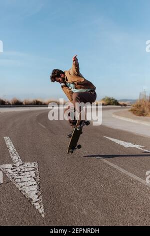 Ganzkörper junge bärtige Skater in casual Outfit springen während Durchführung Kickflip auf Skateboard auf Asphalt Straße Stockfoto