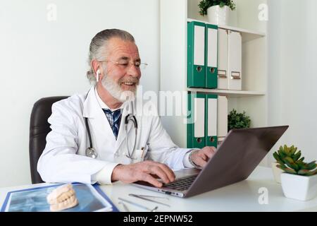 Leitender Kieferorthopäde, der während des Video-Chats gegen Netbook spricht Tisch im Krankenhaus Stockfoto