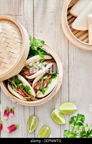 Von oben von leckeren gedämpften Baozi Brötchen mit Rettich und Gurkenscheiben mit Fleisch und frischem Koriander auf dem Tisch Stockfoto