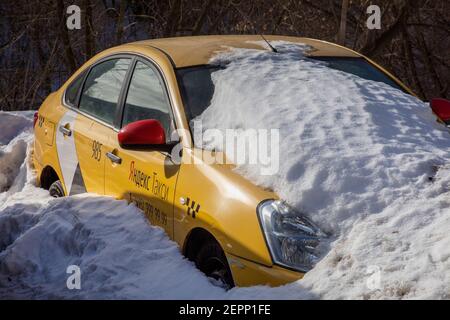 Ein gelbes Taxi mit der Aufschrift "Yandex Taxi" an der Autotür steht unter einem Schnee auf einer Straße in Moskau, Russland Stockfoto