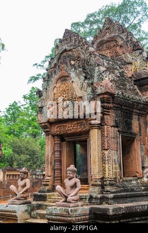 Wächter knien vor den kleinen, aber wunderbar erhaltenen Gebäuden des 10th. Jahrhunderts Tempels von Banteay Srei. Stockfoto