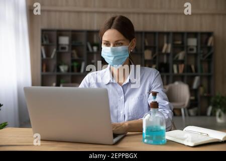 Kaukasische Frau in Facemask Arbeit auf Laptop online Stockfoto