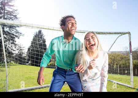 Fußball-Fashion-Geschichte mit einem schwarzen männlichen Modell und Blondine Chinesische weibliche Modell erzielte ein Tor auf einem Fußballplatz Stockfoto