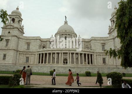 Die Besucher werden im Hintergrund der Victoria Memorial Hall in Kalkutta, Westbengalen, Indien fotografiert. Auf der Spitze der zentralen Kuppel der Halle ist eine Figur des Engels des Sieges, einer Göttin der antiken griechischen Mythologie, die den Sieg verkörpert. Stockfoto