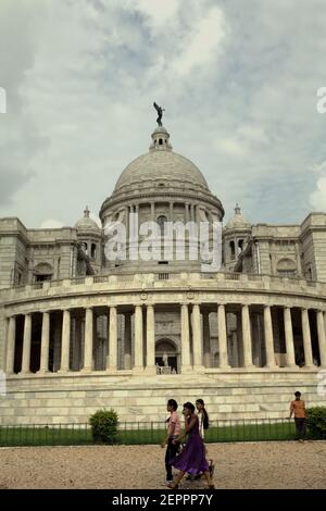 Die Besucher werden im Hintergrund der Victoria Memorial Hall in Kalkutta, Westbengalen, Indien fotografiert. Auf der Spitze der zentralen Kuppel der Halle ist eine Figur des Engels des Sieges, einer Göttin der antiken griechischen Mythologie, die den Sieg verkörpert. Stockfoto