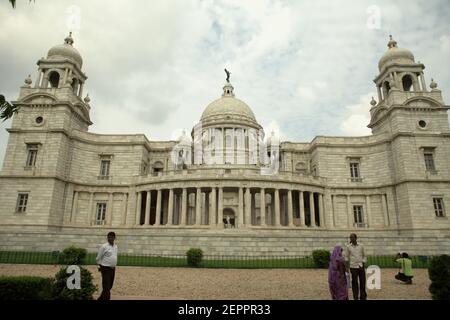 Die Besucher werden im Hintergrund der Victoria Memorial Hall in Kalkutta, Westbengalen, Indien fotografiert. Auf der Spitze der zentralen Kuppel der Halle ist eine Figur des Engels des Sieges, einer Göttin der antiken griechischen Mythologie, die den Sieg verkörpert. Stockfoto