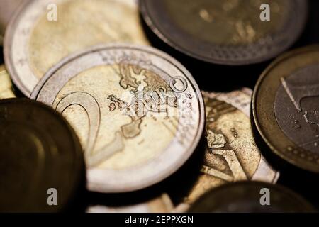Geringe Schärfentiefe (selektiver Fokus) und Makrobild mit einer 2-Euro-Metallmünze in der Nähe anderer Euro-Münzen auf schwarzem Hintergrund. Stockfoto