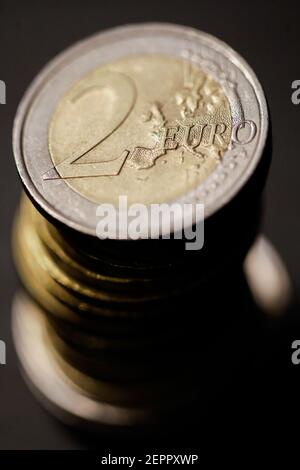 Geringe Schärfentiefe (selektiver Fokus) und Makrobild mit einer 2-Euro-Metallmünze in der Nähe anderer Euro-Münzen auf schwarzem Hintergrund. Stockfoto