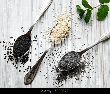 Gesundes Essen und Trinken Konzept. Schwarze und weiße Sesamsamen und Mohnsamen in einem Löffel auf einem Holztisch Stockfoto