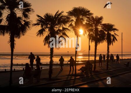 Leute gehen und sitzen entlang der Küste in Southend on Sea, Essex, Großbritannien bei Sonnenuntergang. Abendspaziergang mit bunt niedriger Sonne während COVID 19 Stockfoto