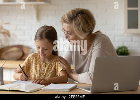 Freundlich gealterte Frau Lehrer beobachten Mädchen Schüler schreiben Mathe Aufgabe Stockfoto