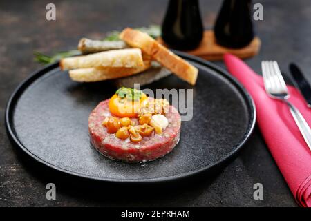 Rindertartare mit Eigelb, eingelegten Pilzen und Senf. Traditionelle Vorspeise. Das Gericht servieren. Stockfoto