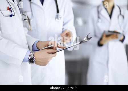 Unbekannte Ärzte, zwei Männer und eine Frau, diskutieren medizinische Untersuchungsresoults, während sie im Krankenhaus-Büro stehen. Ärzte, die Klemmbretter zum Auffüllen verwenden Stockfoto