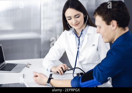 Die junge Ärztin überprüft den Blutdruck ihrer Patientin, während sie zusammen am Schreibtisch in einem Schrank sitzen. Arzt bei der Arbeit in einem Krankenhaus Stockfoto