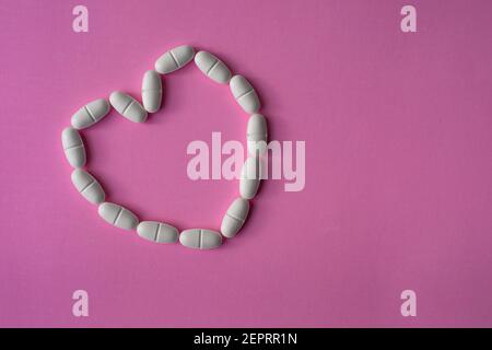 Weiße, große Pillen oder Tabletten, in einer Herzform angeordnet, um Gesundheit auf rosa Hintergrund darstellen Stockfoto