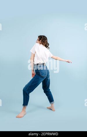 Lebendige zeitgenössische Tänzerin posiert vor blauem Studiohintergrund. Sie bogt leicht ihren Rücken, die Beine sind fest platziert, sodass sie sich verdrehen kann Stockfoto