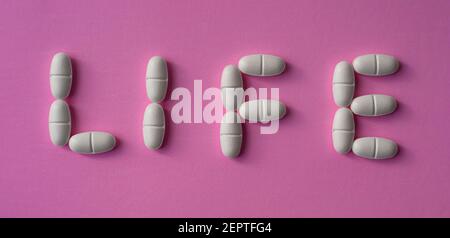 Weiße, große Pillen oder Tabletten mit dem Text "Leben" auf einem rosa Hintergrund angeordnet Stockfoto