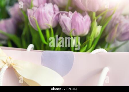 Nahaufnahme Detail von frischen schönen Geschenk von zarten violetten Pfingstrose Tulpen Bouquet und Papier Geschenktüte mit romantischen Schleife. Hochzeit oder Jubiläum Stockfoto