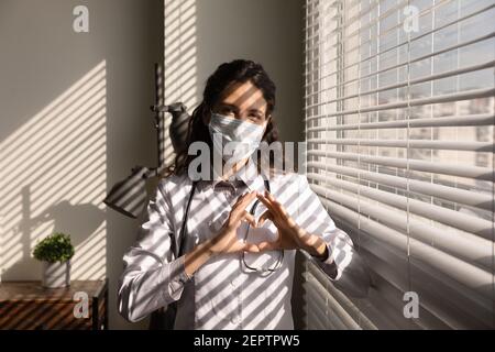 Portrait professionelle Ärztin trägt medizinische Maske zeigt Herz Geste Stockfoto