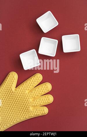 Hitzebeständige Silikonhandschuhe und Schalen auf rotem Hintergrund. Abstraktes Kochkonzept. Flach liegend, Draufsicht mit Kopierplatz Stockfoto