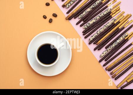 Flache Lage von schwarzer Kaffeetasse und Schokolade getauchten Sticks auf gelbem Hintergrund, Draufsicht mit Kopierraum Stockfoto