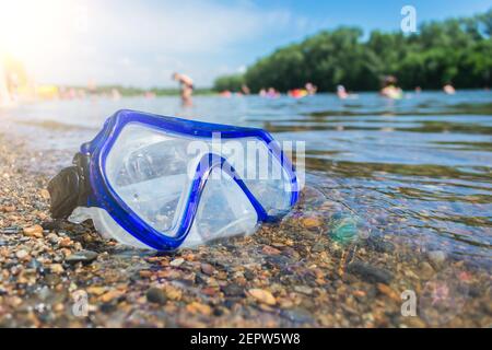 Eine Schwimmmaske liegt an einem öffentlichen Strand in der Nähe des Wasser vor dem Hintergrund der Urlauber Stockfoto