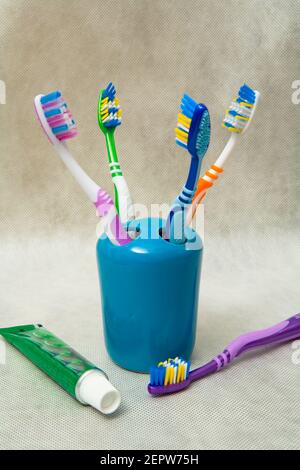 Mehrfarbige Zahnbürsten stehen in einem speziellen Glas neben einer Tube Zahnpasta. Stillleben. Stockfoto