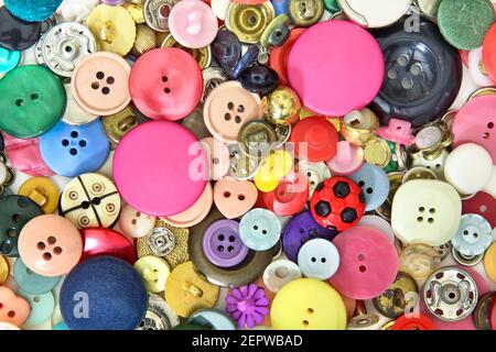 Set von Knöpfen und Nähzubehör in sehr verschiedenen Farben, Größen und Formen. Überwiegend rosa und rot und einige gelbe, blaue und grüne Knöpfe Stockfoto