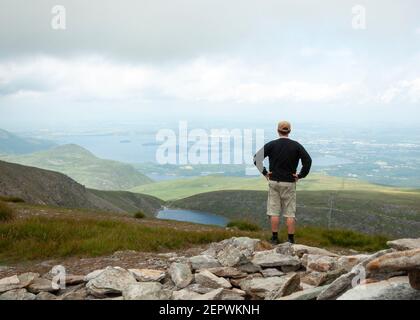 Ein alleinesischer Wanderer auf dem Mangerton Summit mit Blick auf den Devil's Punch Bowl See und die Seen von Killarney beeindruckende Landschaft Grafschaft Kerry, Irland Stockfoto