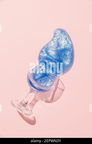 Ein Glas Wein mit kreativem violettem Getränk verschüttet auf einem rosa Hintergrund. Minimalkonzept. Stockfoto