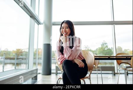 Porträt einer attraktiven jungen Geschäftsfrau, die im Büro auf einem Stuhl sitzt. Gut aussehende weibliche professionelle Blick auf die Kamera und lächelnd. Stockfoto