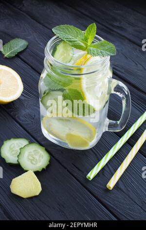 Freche Wasser Abnehmen oder Infused Wasser mit Zitrone, Gurke und Ingwer in das Glas auf dem schwarzen Holzhintergrund. Position vertikal. Stockfoto