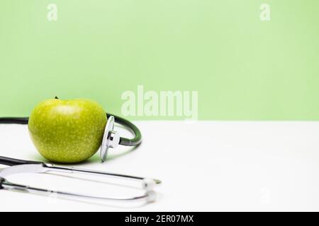 Apfel und Stethoskop auf horizontalem grünen und weißen Hintergrund Stockfoto