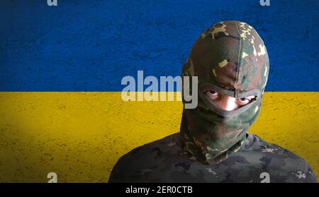ukrainischer wütender Soldat mit ukraine-Flagge dahinter. Militärmann mit Tarnung und wütend aggressiv für den Krieg. Stockfoto
