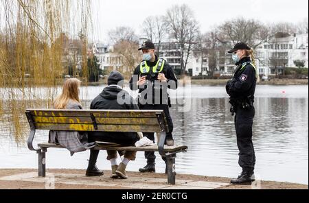 Hamburg, Deutschland. Februar 2021, 28th. Polizeibeamte wenden sich an ein Paar in der Hamburger Außenalster, weil sie auf dem Bakn keinen Mund-Nase-Schutz trugen. Seit gestern hat Hamburg eine strengere Maskenanforderung im öffentlichen Raum. Quelle: Markus Scholz/dpa/Alamy Live News Stockfoto