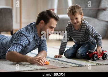 Glücklicher Vater und Sohn Rollen Spielzeugautos auf Heizboden Stockfoto