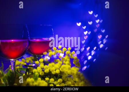 Mimosas und zwei Gläser Rotwein auf einem blauen Hintergrund mit verschwommenen Lichtern in Form von kleinen Herzen Stockfoto