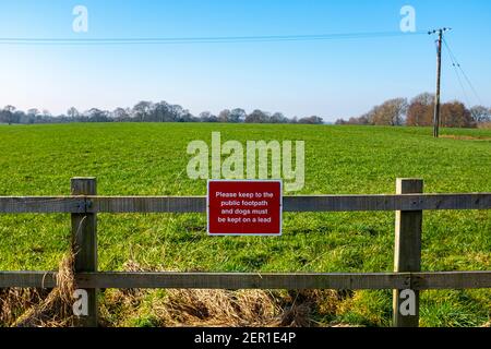 Bitte halten Sie sich an den öffentlichen Fußweg und Hunde müssen sein Auf einem Bleiwarnschild in der Cheshire Landschaft gehalten VEREINIGTES KÖNIGREICH Stockfoto