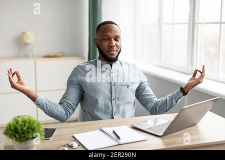 Friedlicher Afrikanischer Geschäftsmann Meditierend Sitzen Am Arbeitsplatz Entspannen Im Büro Stockfoto