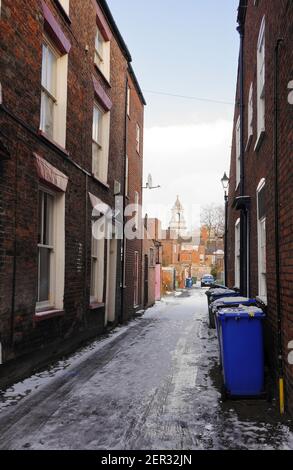 Eine enge, schneebedeckte Straße mit dem hundertjährigen Kirchturm im Hintergrund Stockfoto