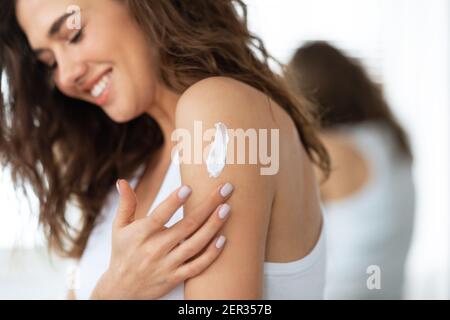 Happy Young Woman Anwendung Feuchtigkeitscreme Auf Körper Stehend Indoor Stockfoto