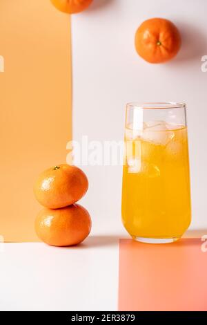Erfrischendes Mandarinengetränk mit Eis in einer Lasse auf weißem und orangenen Hintergrund mit frischem Mandarinenstapel. Minimalismus und Balance Konzept. Stockfoto