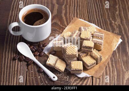 Tasse heißen Kaffee und kleine Schokoladenwaffeln auf alten Holztisch Stockfoto