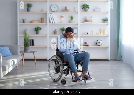 Depression und Einsamkeit bei behinderten Erwachsenen. Junge schwarze Kerl im Rollstuhl weinend im Wohnzimmer, kopieren Raum Stockfoto