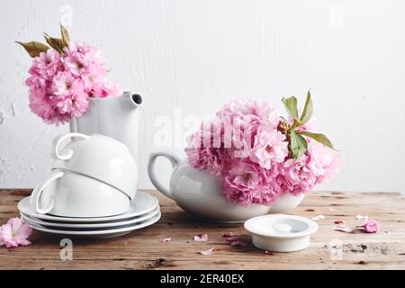 Weiße Tassen, Teekanne und rosa japanische Kirschblüten. Stillleben im Frühling. Stockfoto