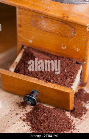 Teilansicht einer manuellen Kaffeemühle aus Holz mit einer offenen Schublade und verstreutem gemahlenem Kaffeepulver. Stockfoto