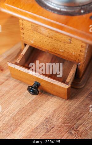 Teilansicht der manuellen hölzernen Kaffeemühle mit offener Schublade auf abgenutztem Holzboden. Stockfoto