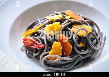 Nahaufnahme eines Tellers mit Spaghetti Tintenfisch Tinte Scheiben von Bottarga und Chili Stockfoto